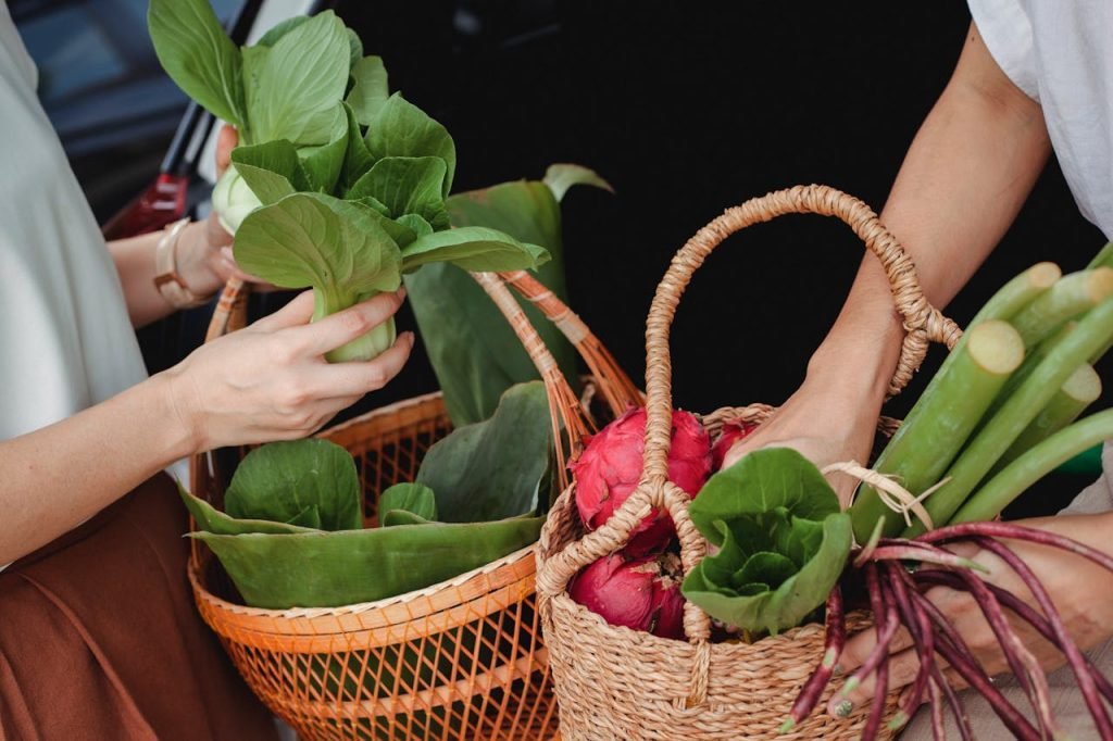 fresh-green-vegetables-on-woven-basket-5709305 Close-up of hands holding wicker baskets filled with fresh vegetables and fruits outdoors.
